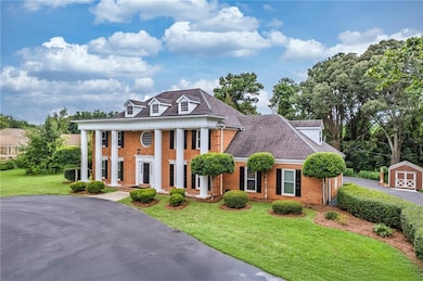 Greek revival inspired property with a front lawn, a porch, brick siding, and roof with shingles