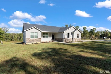 View of front facade featuring stone siding, a front yard, and a shingled roof