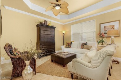 Living area with a ceiling fan, a tray ceiling, baseboards, ornamental molding, and light tile patterned flooring