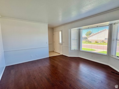 Spare room with dark wood-type flooring, crown molding, and a textured ceiling