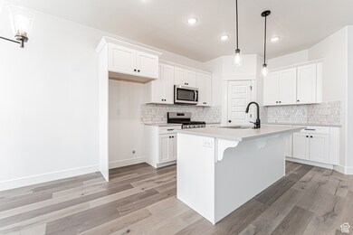 Kitchen featuring appliances with stainless steel finishes, white cabinetry, light countertops, light wood finished floors, and recessed lighting