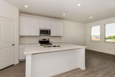 Kitchen with an island with sink, white cabinetry, hardwood / wood-style floors, and stainless steel appliances
