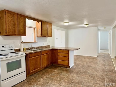 Kitchen featuring white electric range, a peninsula, brown cabinetry, and a textured ceiling