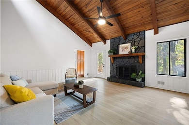 Living room with light wood finished floors, a fireplace, a wood ceiling with exposed beams, high vaulted ceiling, and a ceiling fan