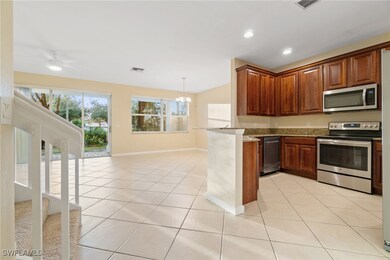 Kitchen featuring appliances with stainless steel finishes, open floor plan, a chandelier, light tile patterned flooring, and light stone counters