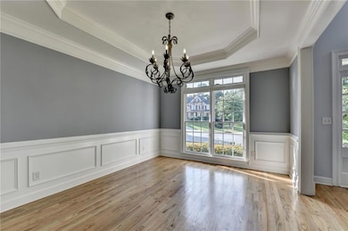 Spare room with ornamental molding, a chandelier, wood finished floors, a wainscoted wall, and a raised ceiling