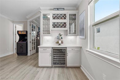 Bar featuring wine cooler, baseboards, a bar, ligh
