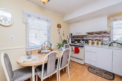 Kitchen with white cabinets, white electric stove, light countertops, decorative backsplash, and light wood-style floors