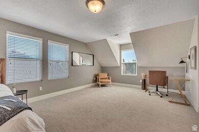 Bedroom featuring a textured ceiling, light colored carpet, lofted ceiling, and a desk