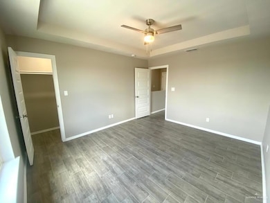 Unfurnished bedroom featuring a tray ceiling, wood finished floors, and a ceiling fan