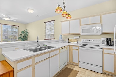 Kitchen featuring white appliances, a ceiling fan, light countertops, and decorative light fixtures