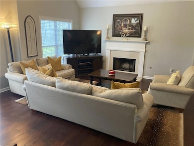 Living area featuring a fireplace with raised hearth, lofted ceiling, and dark wood finished floors