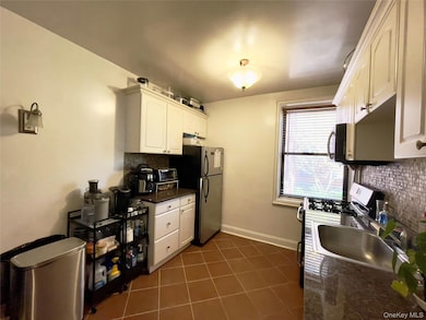 Kitchen featuring tasteful backsplash, dark tile patterned flooring, stainless steel appliances, white cabinets, and dark stone counters