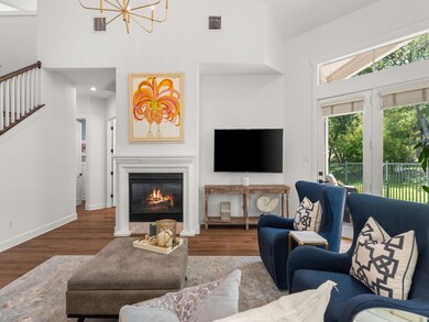Living room featuring wood finished floors, a glass covered fireplace, a chandelier, high vaulted ceiling, and stairway