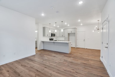 Kitchen featuring white cabinetry, a peninsula, decorative light fixtures, light wood-type flooring, and a chandelier