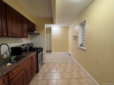 Kitchen featuring stainless steel appliances, dark stone countertops, light tile patterned flooring, under cabinet range hood, and baseboard heating