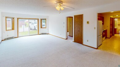 Empty room with a baseboard heating unit, carpet, ceiling fan, and a textured ceiling