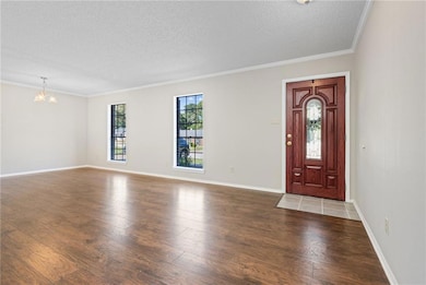 Foyer entrance featuring ornamental molding, dark wood finished floors, a chandelier, and a textured ceiling