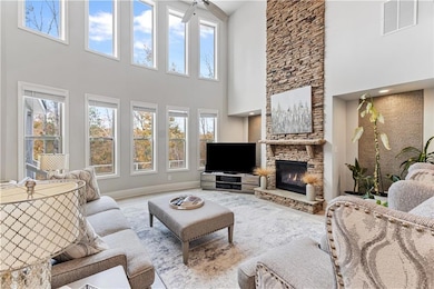 Living room with a stone fireplace, wood finished floors, healthy amount of natural light, and a towering ceiling