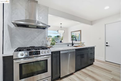 Kitchen with wall chimney range hood, stainless steel appliances, dark cabinetry, light wood finished floors, and backsplash