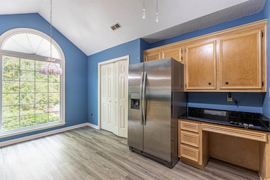 Kitchen featuring light wood finished floors, visible vents, baseboards, lofted ceiling, and stainless steel refrigerator with ice dispenser