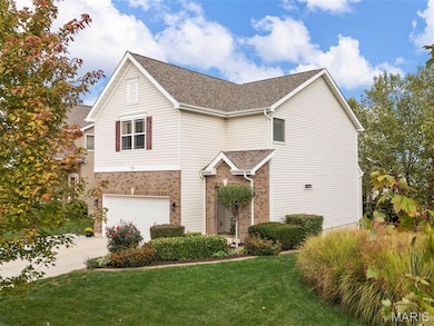 Traditional-style house featuring brick siding, a front yard, a shingled roof, driveway, and an attached garage