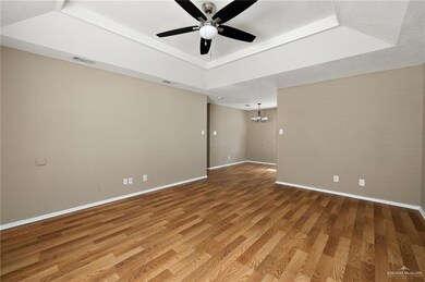 Spare room with a tray ceiling, a textured ceiling, wood-type flooring, and ceiling fan with notable chandelier