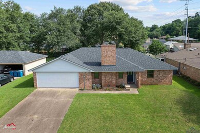 View of front of property with roof with shingles, a chimney, brick siding, concrete driveway, and a front lawn