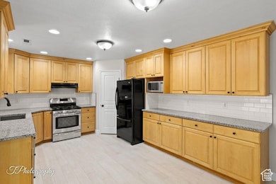 Kitchen with light stone counters, decorative backsplash, appliances with stainless steel finishes, light brown cabinets, and recessed lighting