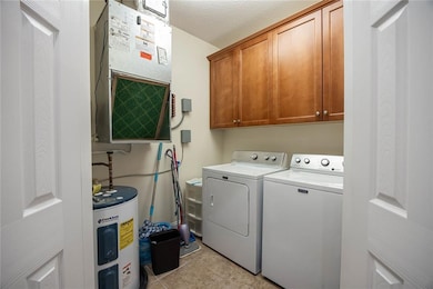 Washroom featuring electric water heater, cabinet space, light tile patterned flooring, a textured ceiling, and washing machine and clothes dryer
