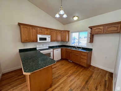 Kitchen featuring brown cabinets, white appliances, dark countertops, decorative light fixtures, and light wood-style flooring