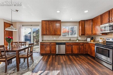 Kitchen featuring stainless steel appliances, dark wood-style floors, light stone counters, and brown cabinets