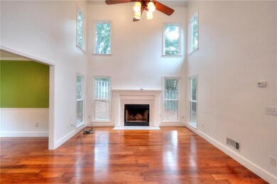 Living room featuring a ceiling fan, a tile fireplace, a towering ceiling, and wood finished floors.