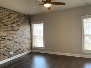 Empty room featuring dark wood finished floors, a ceiling fan, and brick wall