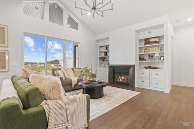 Living room featuring high vaulted ceiling, a fireplace with flush hearth, wood finished floors, built in shelves, and a chandelier