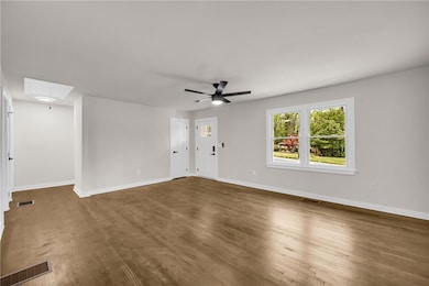 Unfurnished living room featuring attic access, wood finished floors, and ceiling fan