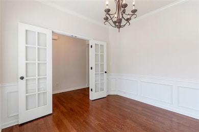 Unfurnished dining area with a chandelier, ornamental molding, french doors, dark wood-type flooring, and a wainscoted wall