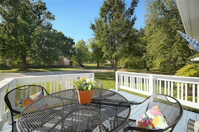 Wooden terrace with outdoor dining space, a yard, and view of trees