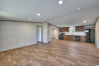 Kitchen featuring light countertops, wood finished floors, a textured ceiling, open floor plan, and black appliances