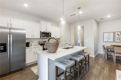 Kitchen with appliances with stainless steel finishes, a kitchen breakfast bar, white cabinetry, decorative backsplash, and dark wood-style flooring