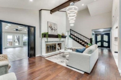 Living room with french doors, beamed ceiling, wood finished floors, a glass covered fireplace, and stairs