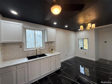 Kitchen with tasteful backsplash, white cabinets, recessed lighting, light stone counters, and a chandelier