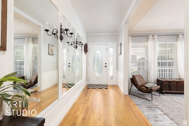 Foyer featuring wood finished floors, ornamental molding, a decorative wall, and a wainscoted wall