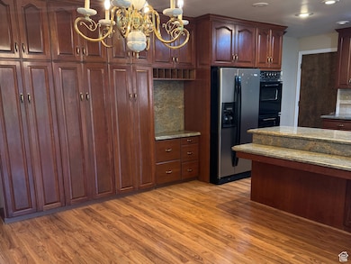 Kitchen with light wood-type flooring, a chandelier, black appliances, light stone countertops, and decorative light fixtures