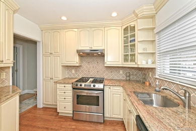 Kitchen with cream cabinetry, stainless steel range with gas cooktop, glass insert cabinets, dark wood-style floors, and tasteful backsplash