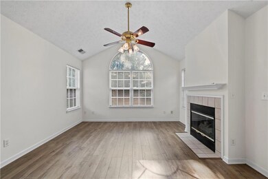 Unfurnished living room featuring ceiling fan, wood finished floors, a textured ceiling, a fireplace, and vaulted ceiling