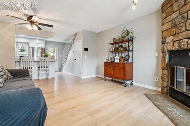 Living room featuring light wood finished floors, a stone fireplace, a ceiling fan, baseboards, and stairway