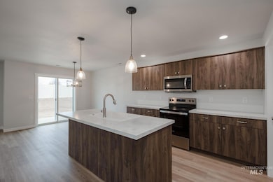 Kitchen with stainless steel appliances, light countertops, pendant lighting, dark brown cabinets, and light wood finished floors