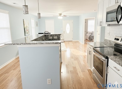 Kitchen featuring stainless steel appliances, light wood-type flooring, dark stone counters, hanging light fixtures, and a kitchen island with sink