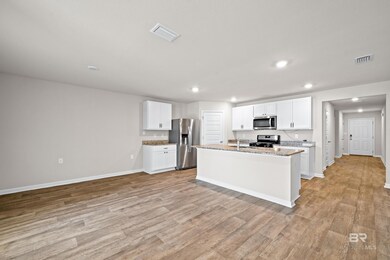 Kitchen with light hardwood / wood-style floors, a kitchen island with sink, light stone counters, stainless steel appliances, and white cabinetry